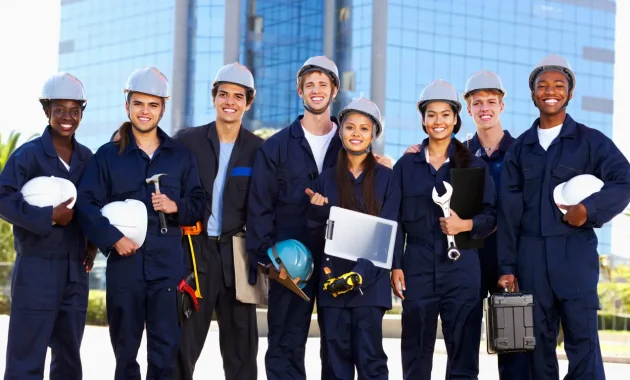 A diverse group of young, smiling South African professionals in work uniforms, holding tools and standing in front of a modern building. They look happy and motivated, with a bright sunny background. The image should feel inspiring, professional, and engaging